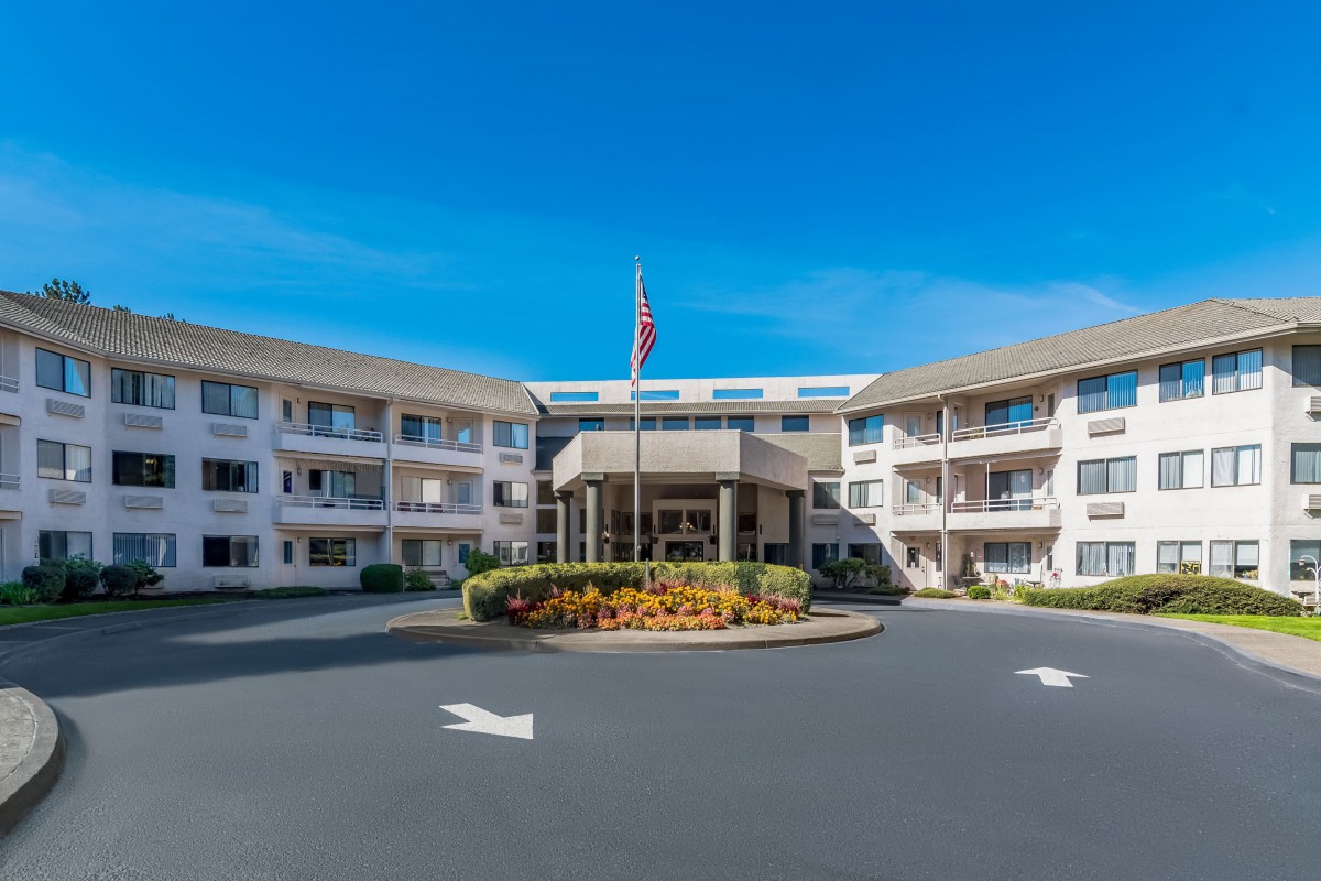 A hotel entrance with a circular driveway and manicured landscaping, featuring a flag in front.