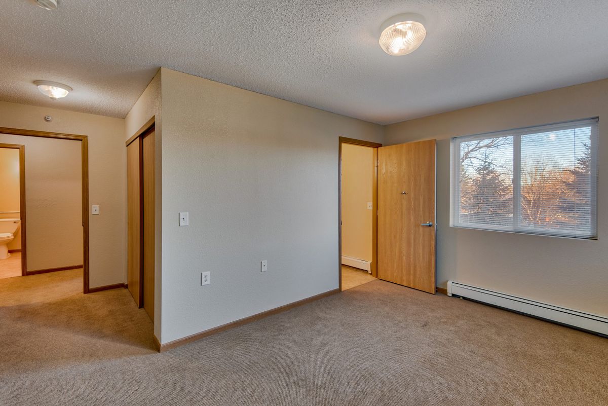 An empty room with carpeted flooring, a window, and open doors.