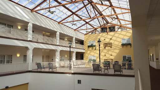 A spacious atrium featuring a glass roof and wooden beams, designed with balconies and seating areas.