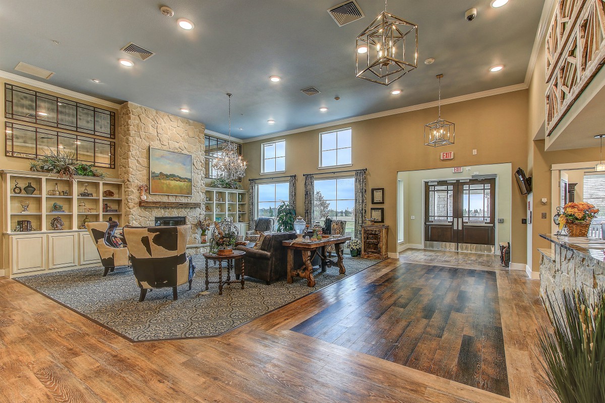 A spacious and cozy living room with wood flooring, elegant chandeliers, and a warm fireplace.