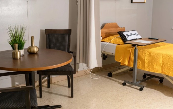 A hospital room featuring a medical bed, a table with chairs, and a curtain for privacy.