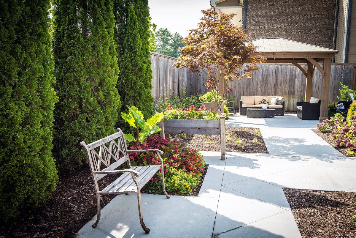 A beautifully landscaped garden with a bench, raised plant beds, and a patio area.