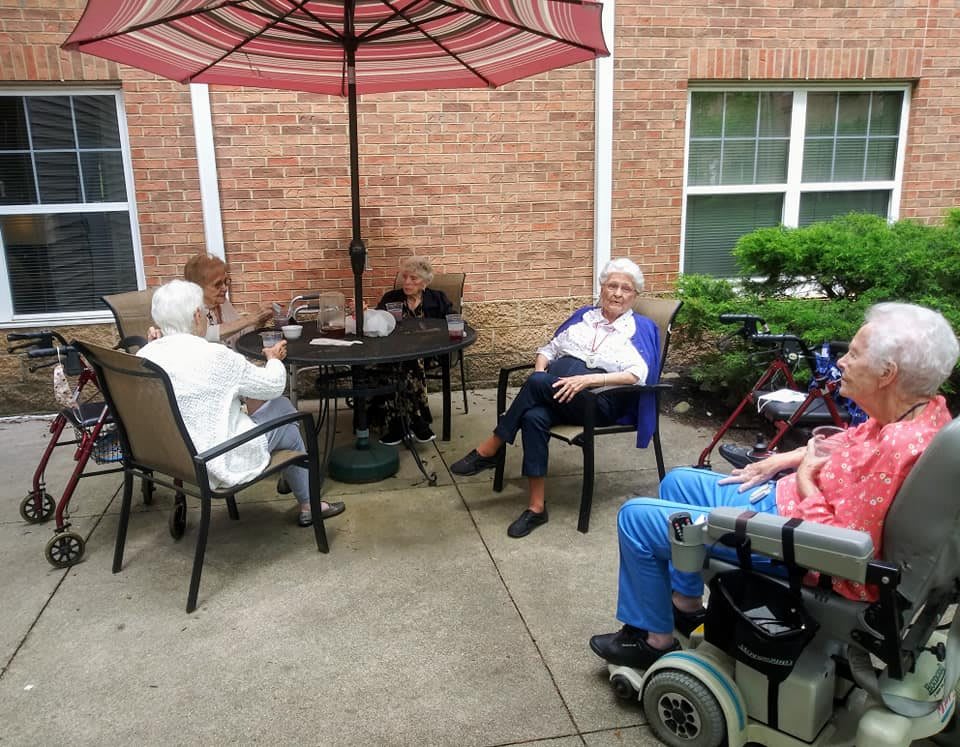 A group of seniors sitting outdoors on a patio, enjoying the day under an umbrella.