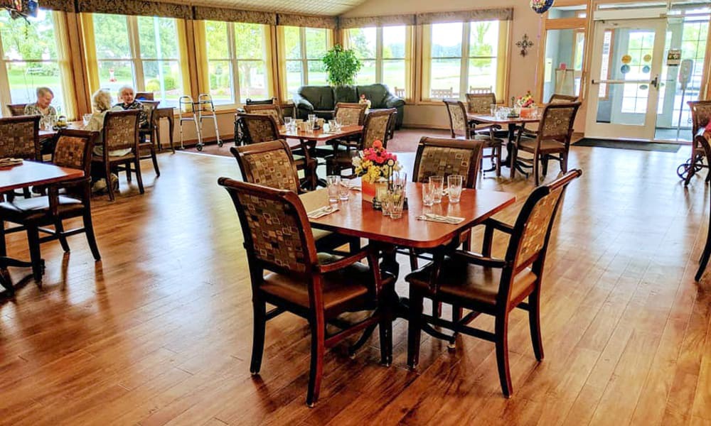 A cozy dining room with neatly arranged tables and chairs, featuring large windows that brighten the space.