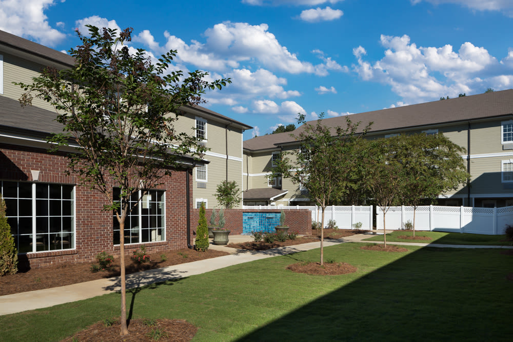 A view of apartment buildings with a well-maintained lawn and trees under a clear sky.