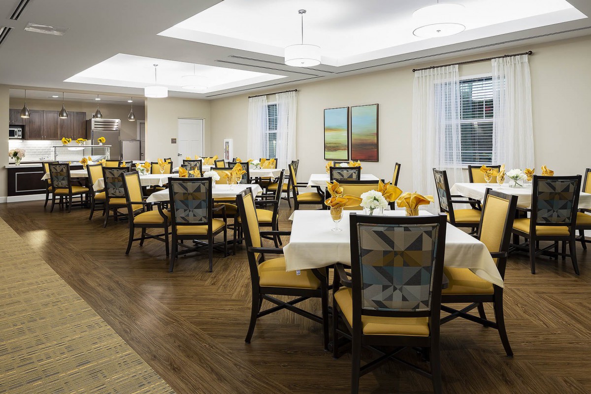 A well-lit dining room with multiple tables and chairs, featuring elegant decor and wooden flooring.