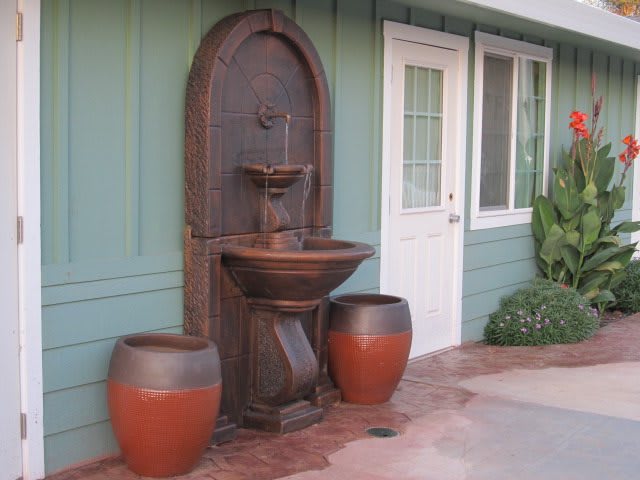 An outdoor wall-mounted fountain accompanied by two large pots on a patio.