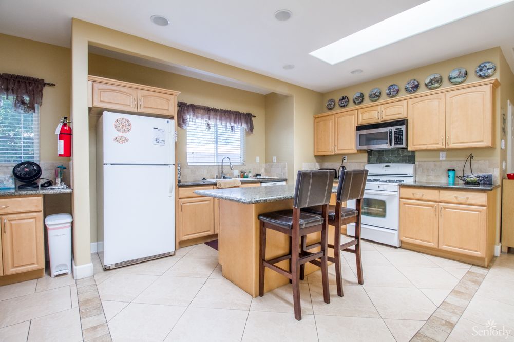 A modern kitchen interior featuring an island with stools, wooden cabinets, a white fridge, and an oven.