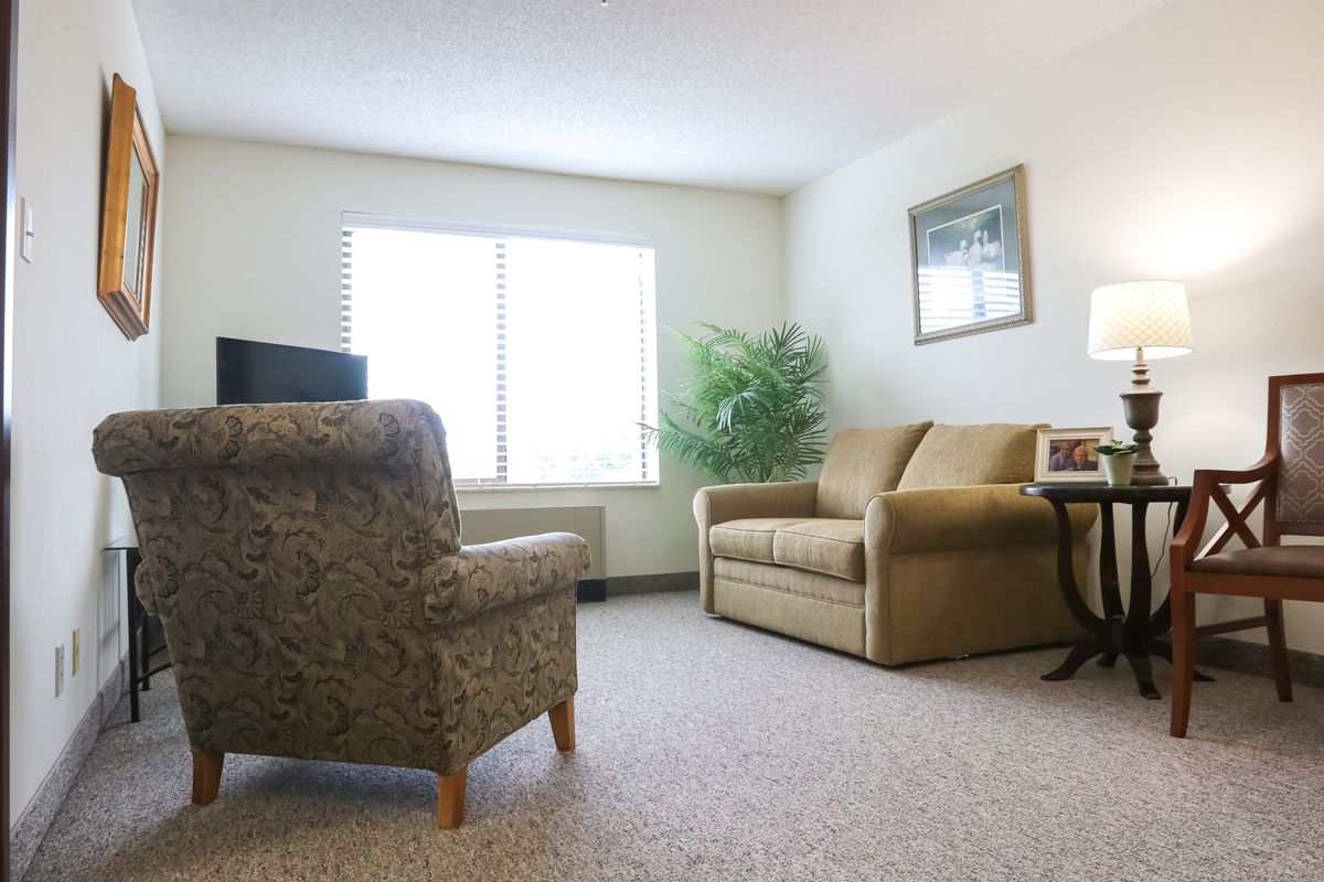 A cozy living room with a sofa, armchair, and window allowing natural light.