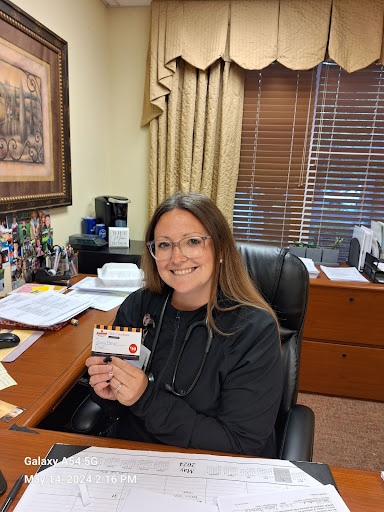 A woman smiling while holding a card at her office desk.