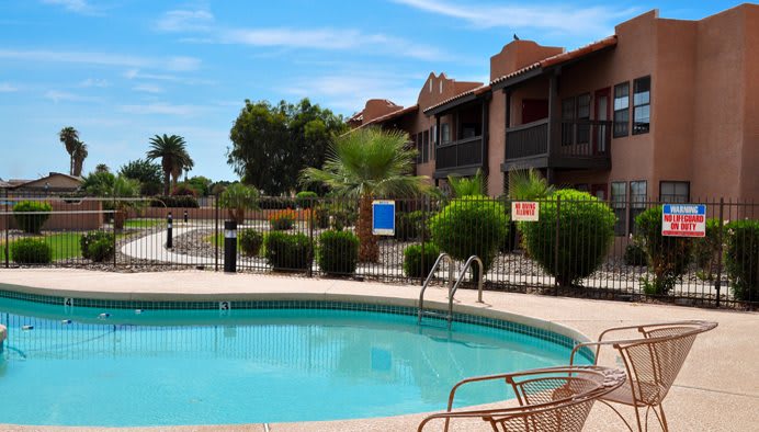 A serene apartment complex with a crystal-clear swimming pool on a sunny day.