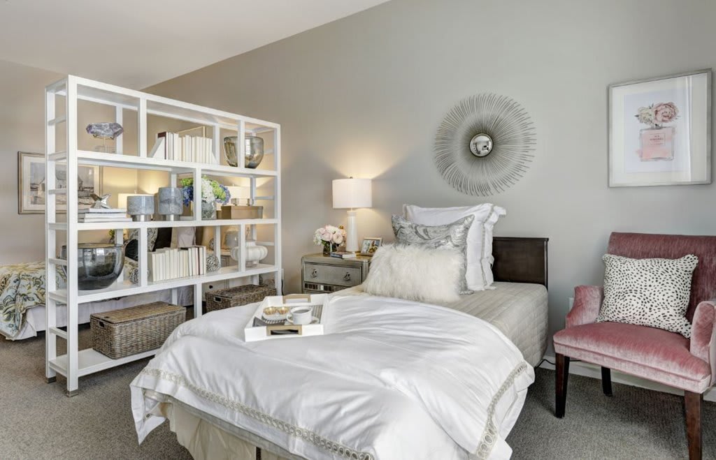 A modern bedroom with stylish decor, featuring a comfortable bed, a shelving unit, and elegant lighting.