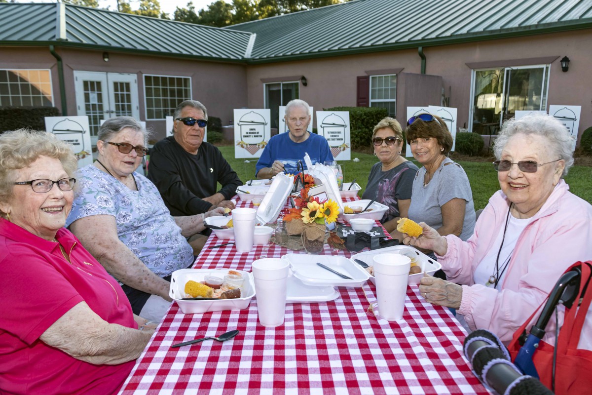 A group of adults enjoying a picnic together at an outdoor table with food and drinks.