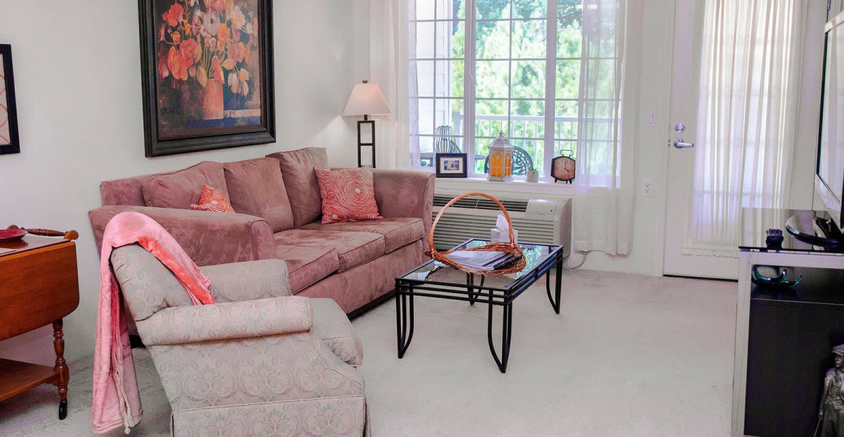 A cozy living room with a pink sofa, glass coffee table, and large window letting in natural light.