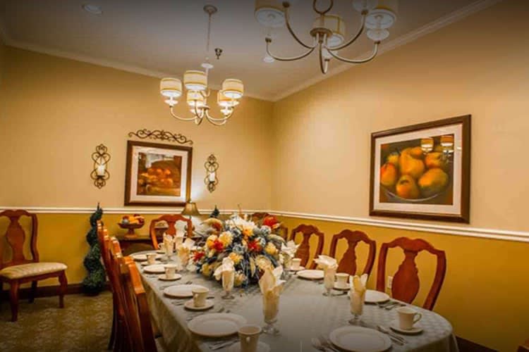An elegantly set dining room with a large table, surrounded by chairs and adorned with a beautiful flower centerpiece. The room is illuminated by a chandelier and decorated with wall art.