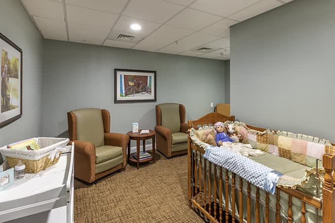A cozy nursery room with two rocking chairs, a side table, and a crib.