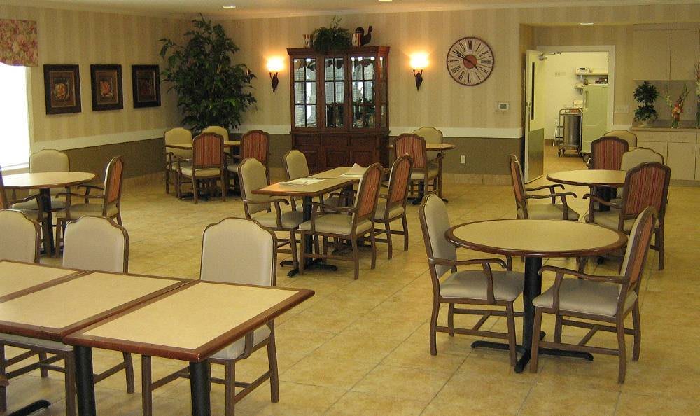 An empty dining area with several tables and chairs, featuring a wall clock and a wooden cabinet.