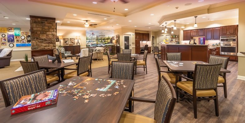 An empty dining room with neatly arranged tables and chairs, featuring a partially completed puzzle on one table.