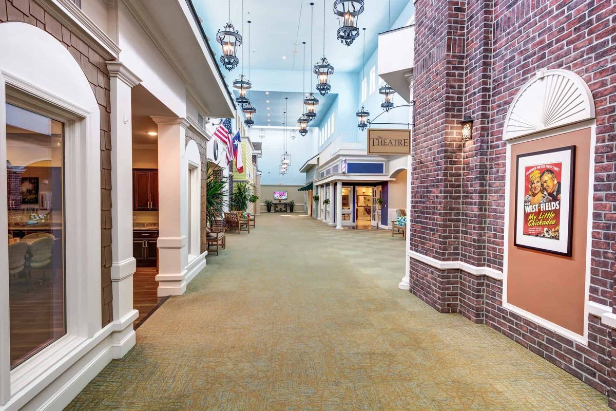 A spacious indoor shopping mall hallway with various stores, flags, and decorative lighting.
