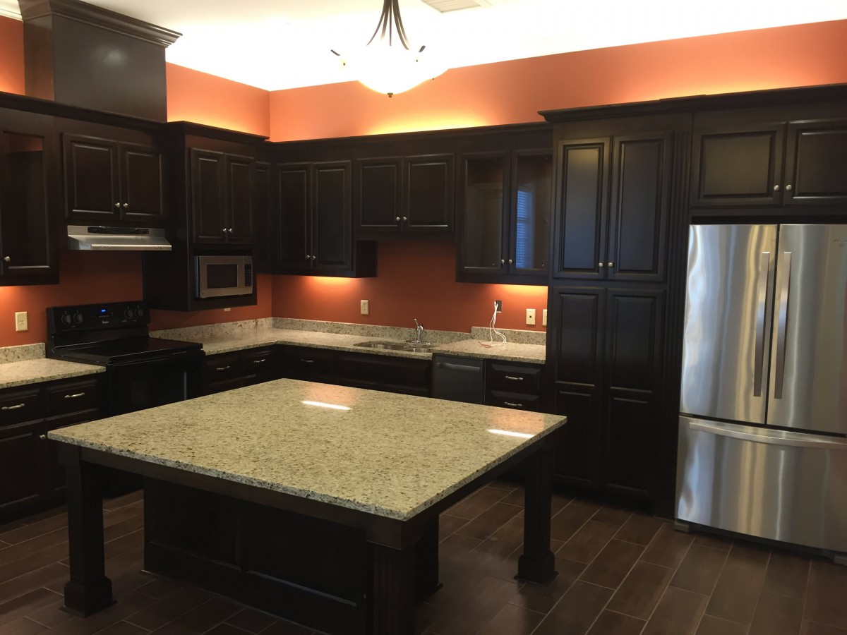 A modern kitchen with dark cabinets, a granite island, and stainless steel appliances.