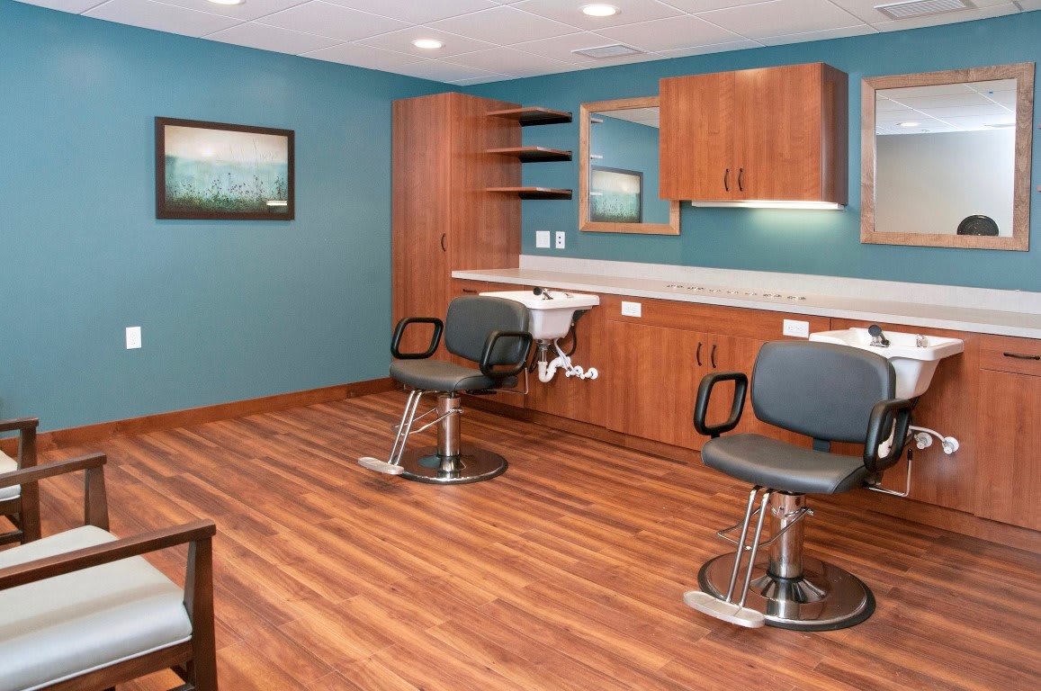 A modern salon interior with two barber chairs, a sink, and wooden cabinetry on a hardwood floor.