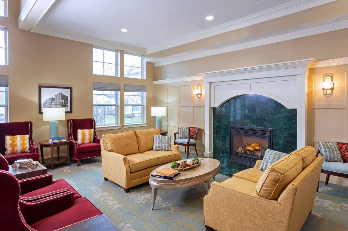 A cozy living room with beige sofas and a fireplace, featuring a modern coffee table and ample natural light from large windows.