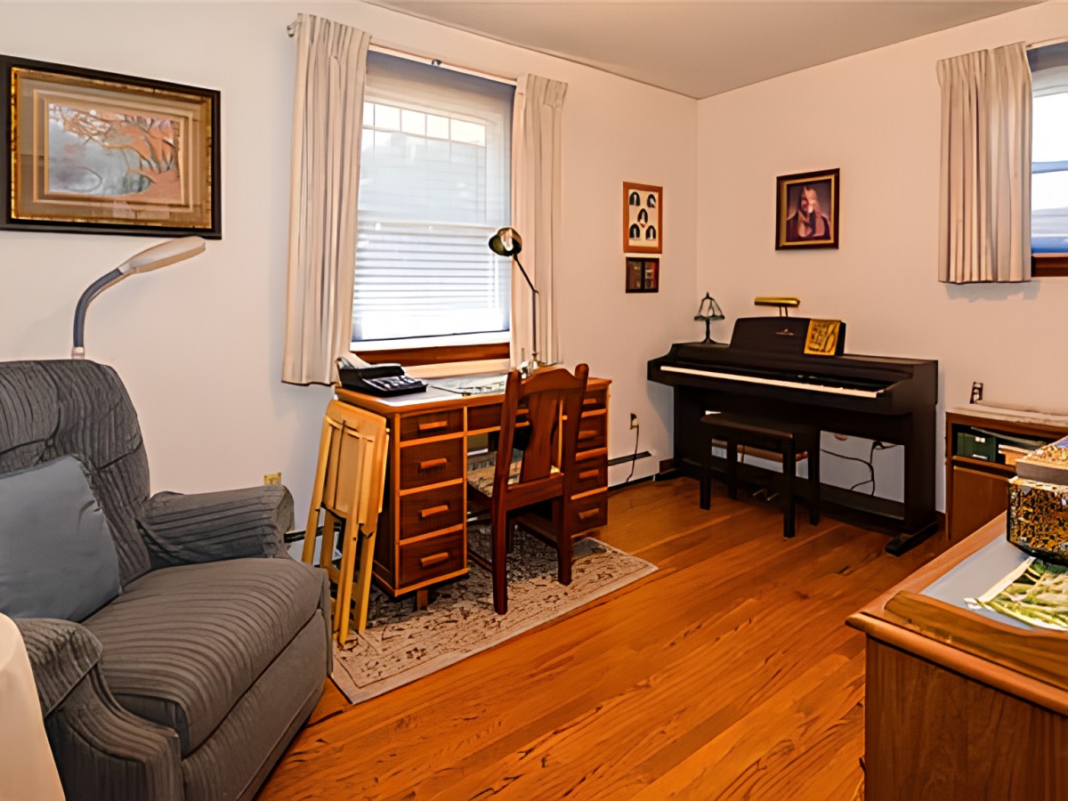 A cozy home office featuring a desk, chair, piano, and wall art.