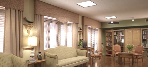 A cozy living room featuring a light-colored sofa, window blinds, and a desk in a well-lit space.