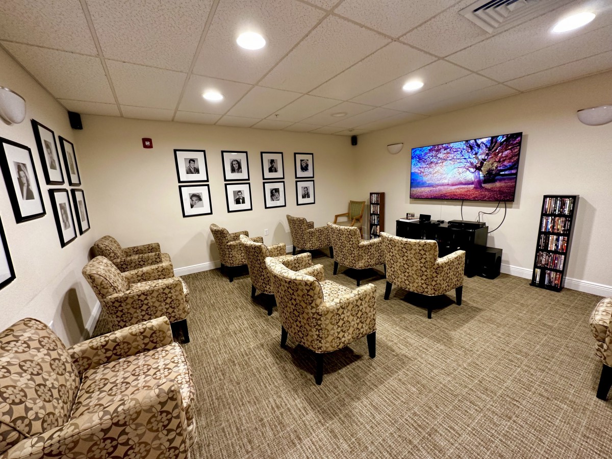 A cozy seating area with armchairs facing a large television, decorated with framed wall art and warm lighting.