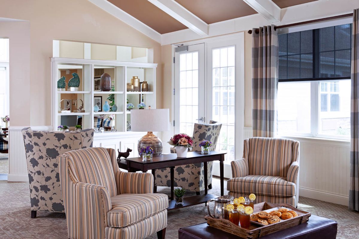 A cozy living room featuring striped chairs, decorative shelves, and a bright window with curtains.
