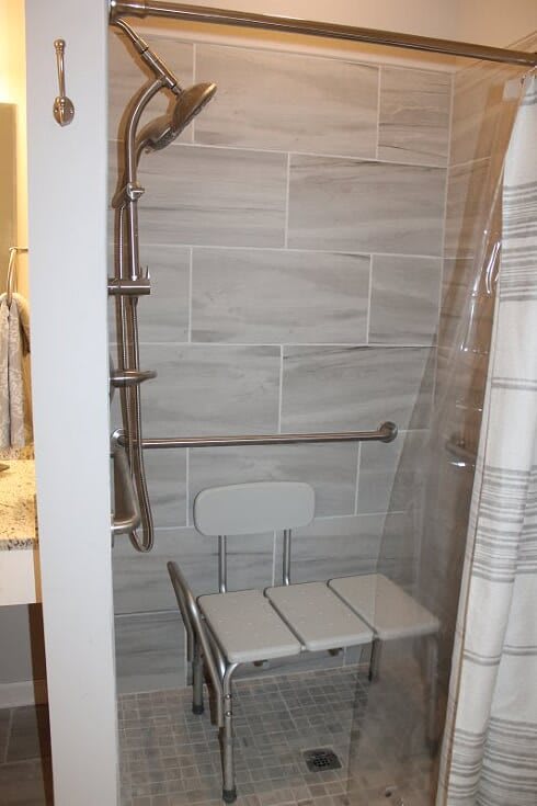 An accessible shower with grab bars and a shower chair, featuring a tiled wall.