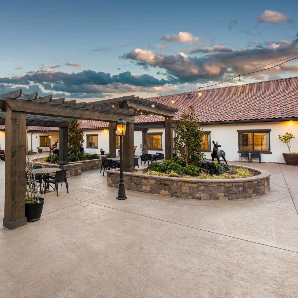 A beautifully landscaped outdoor courtyard with a pergola and seating area under a cloudy sky.