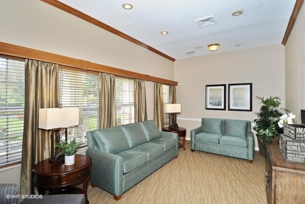 A cozy living room with green sofas, decorative lamps, and large windows with curtains.