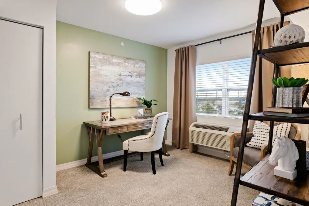 A cozy home office with a green accent wall, featuring a stylish desk, chair, and large window.