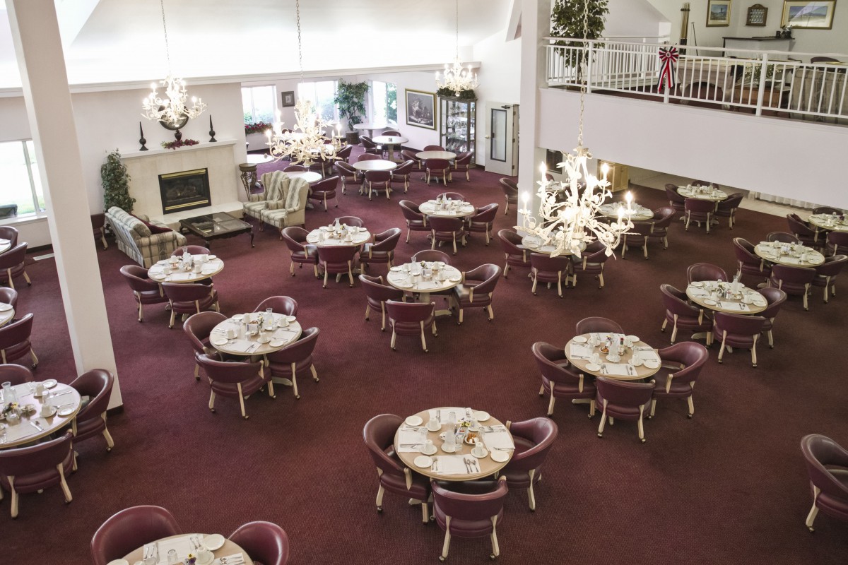 An elegant restaurant dining area with multiple round tables and chairs, adorned with chandeliers and a carpeted floor.