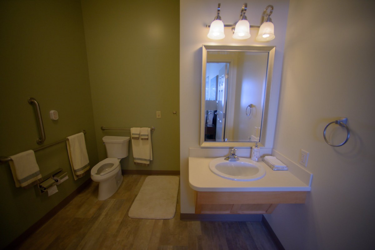 A modern bathroom with a sink, mirror, and toilet, featuring stylish lighting and tile flooring.