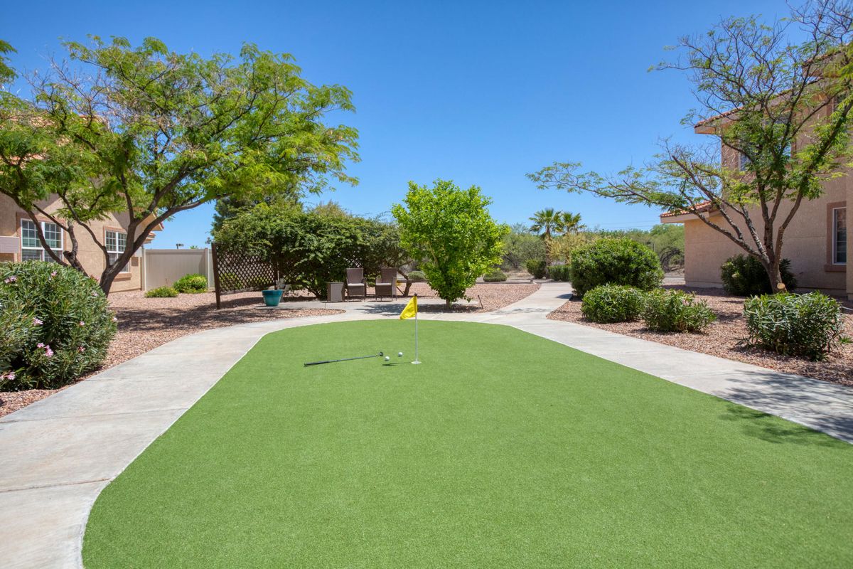 An outdoor mini golf putting green surrounded by trees on a sunny day.