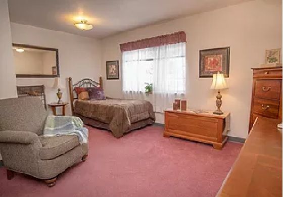 A cozy bedroom with a single bed and armchair, featuring warm decor and natural light from the window.