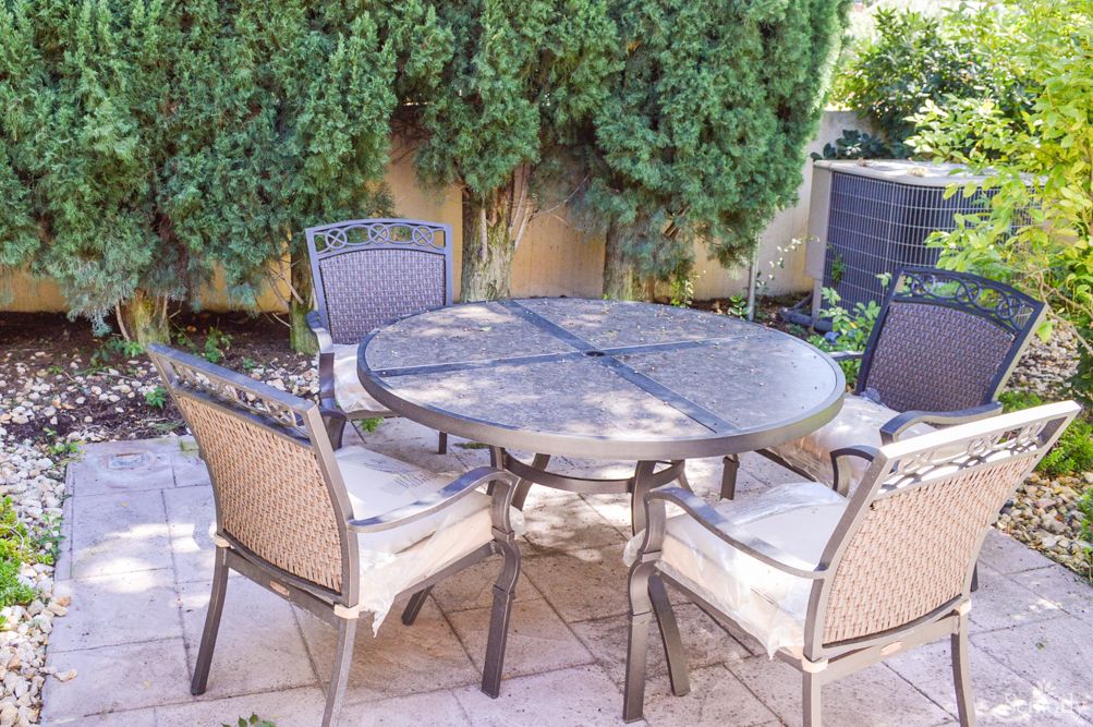 A cozy outdoor patio setup with a round table and four chairs surrounded by lush greenery.