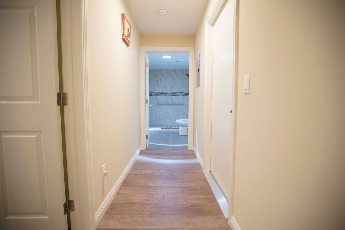 A narrow hallway with wooden flooring leads to a bathroom at the end.