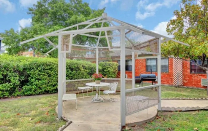A cozy outdoor gazebo with a table and chairs, set amidst a lush garden.