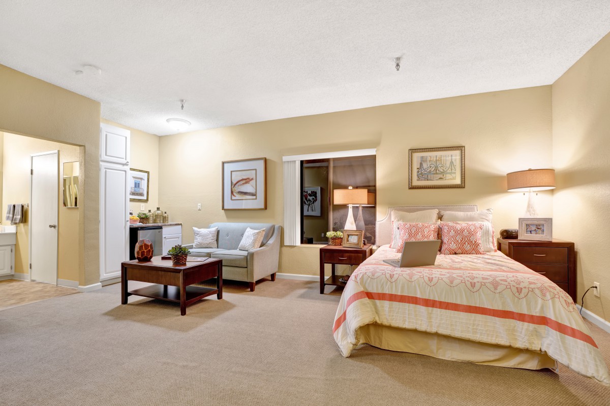 A cozy bedroom featuring a bed with striped bedding, a sofa, and decorative elements like lamps and framed pictures.