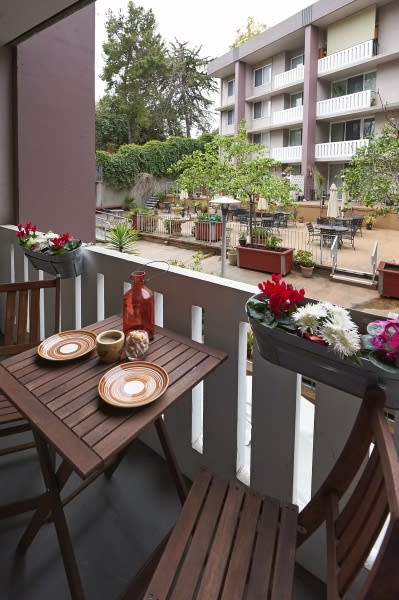 A cozy balcony setup with wooden furniture and decorative flowers overlooking a garden area.