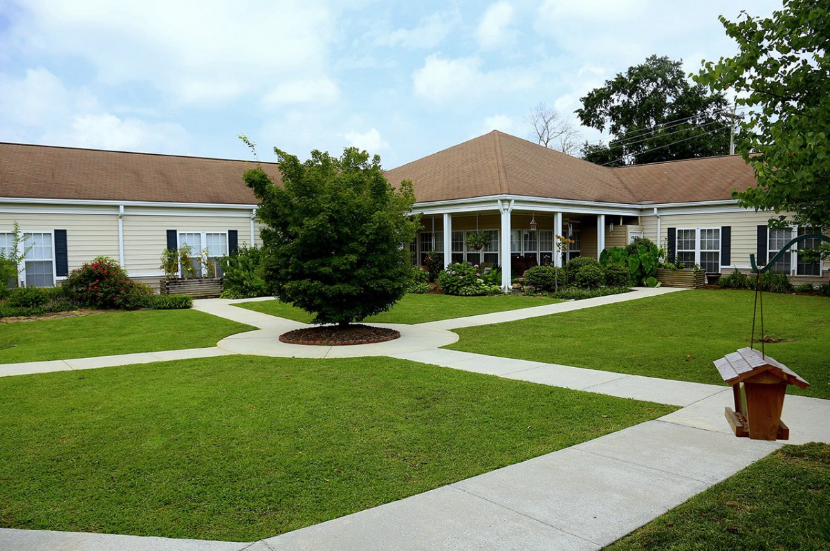 A building with a well-manicured lawn, intersecting pathways, and surrounding trees under a partly cloudy sky.