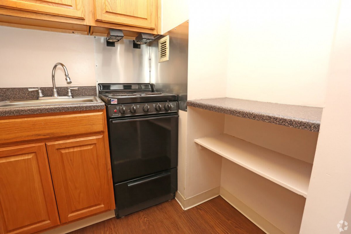 A compact apartment kitchen with a stove, sink, and shelving.