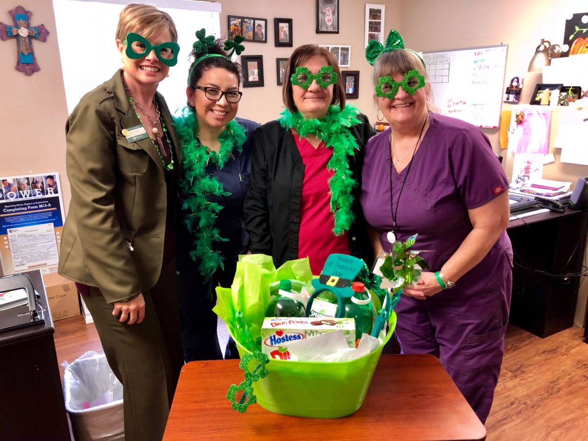 A group of people dressed in green costumes and accessories celebrating St. Patrick's Day around a festive basket.