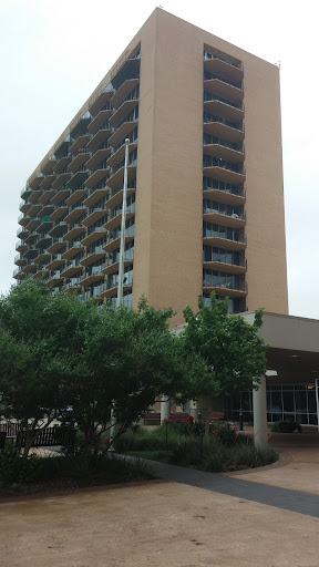 A tall apartment building featuring multiple balconies, set against a cloudy sky.
