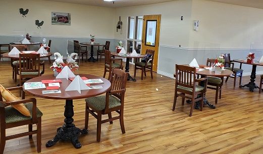 A neatly arranged dining area with wooden tables and chairs, adorned with folded napkins.