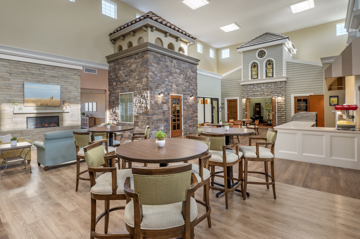A spacious interior with a modern seating area featuring tables and chairs, surrounded by decorative stone elements and high ceilings.