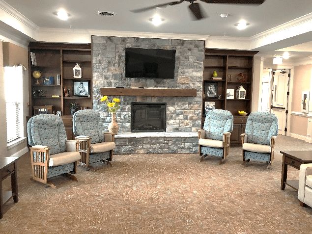 A cozy living room with four armchairs arranged around a stone fireplace and a television, flanked by dark wooden bookshelves.